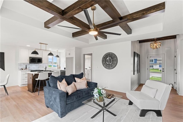 living room featuring coffered ceiling, beamed ceiling, light wood-style floors, ceiling fan with notable chandelier, and baseboards