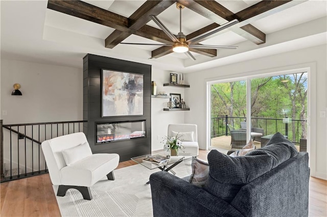 living room with beamed ceiling, coffered ceiling, wood finished floors, and a glass covered fireplace