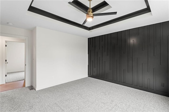 empty room with baseboards, a raised ceiling, ceiling fan, and carpet flooring