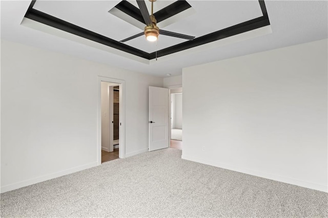 empty room featuring a ceiling fan, a tray ceiling, carpet, and baseboards