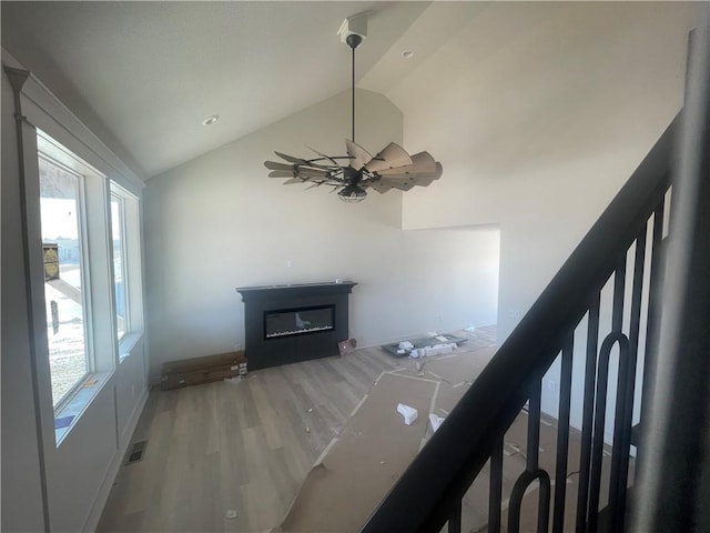 unfurnished living room featuring a glass covered fireplace, visible vents, vaulted ceiling, and wood finished floors