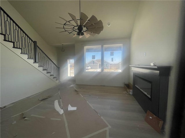 unfurnished living room featuring a glass covered fireplace, ceiling fan, and stairs