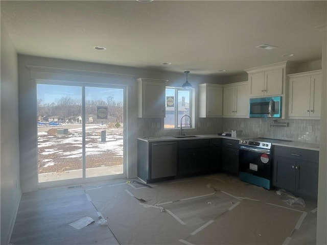 kitchen with stainless steel appliances, light countertops, backsplash, white cabinetry, and a sink