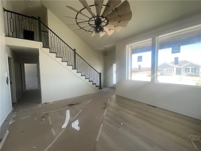 unfurnished living room with ceiling fan, a high ceiling, wood finished floors, visible vents, and stairs