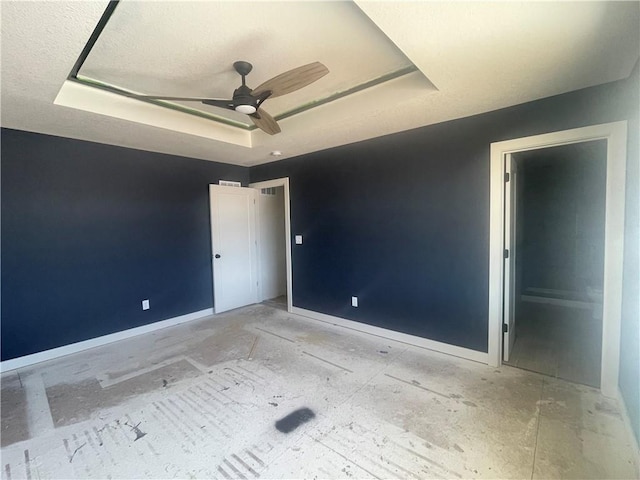 empty room featuring a ceiling fan, a tray ceiling, and baseboards