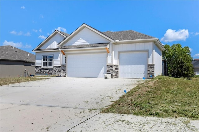 view of front of home featuring driveway, a shingled roof, stone siding, an attached garage, and board and batten siding