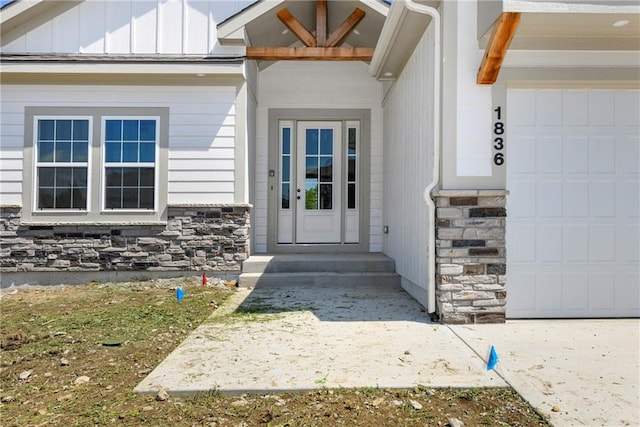 view of exterior entry with stone siding, board and batten siding, and an attached garage