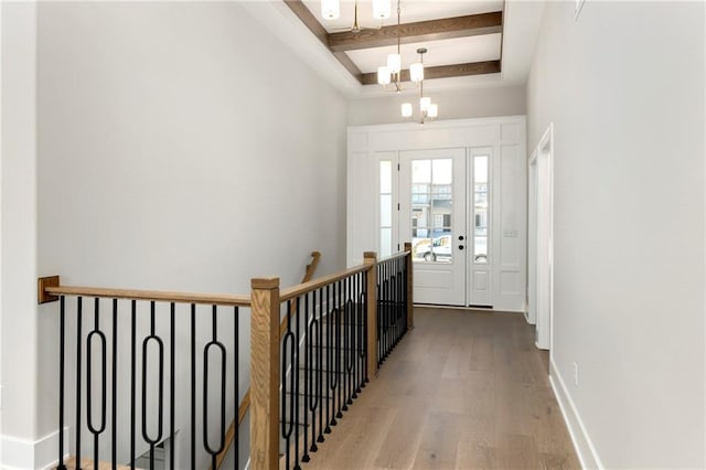 hall with a tray ceiling, beam ceiling, a notable chandelier, wood finished floors, and baseboards