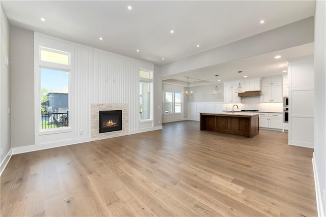 unfurnished living room featuring light wood finished floors, recessed lighting, a sink, a lit fireplace, and baseboards