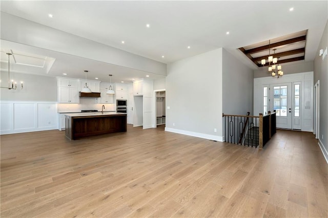 unfurnished living room featuring baseboards, a tray ceiling, light wood-style floors, a notable chandelier, and recessed lighting