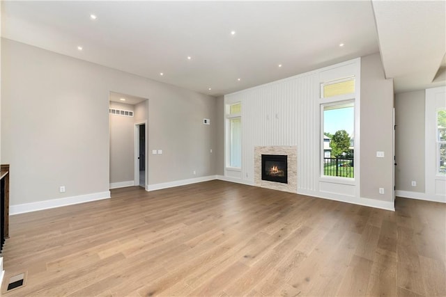 unfurnished living room with light wood finished floors, baseboards, visible vents, and a glass covered fireplace