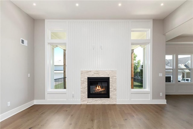 unfurnished living room with baseboards, visible vents, wood finished floors, and a glass covered fireplace