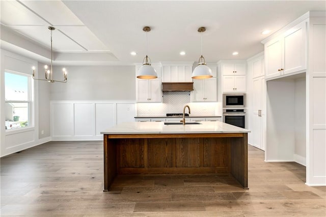 kitchen featuring tasteful backsplash, white cabinets, oven, built in microwave, and a sink