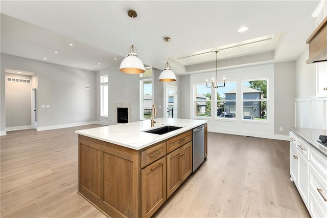 kitchen featuring light wood-style flooring, a sink, brown cabinets, dishwasher, and a raised ceiling