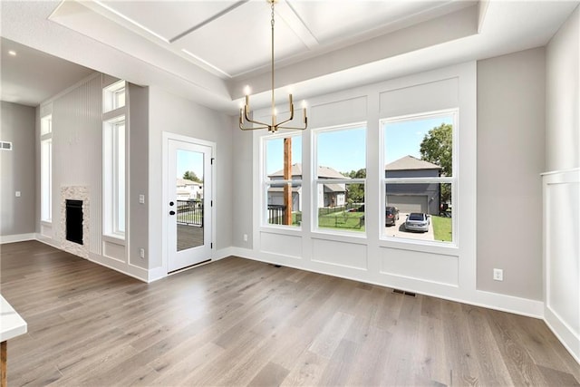 unfurnished dining area with visible vents, a healthy amount of sunlight, a stone fireplace, and wood finished floors