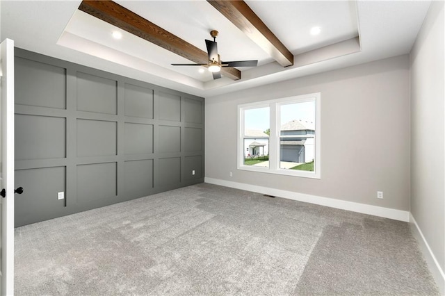 unfurnished bedroom featuring a decorative wall, baseboards, beamed ceiling, carpet, and a raised ceiling