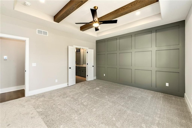 unfurnished bedroom featuring a decorative wall, visible vents, beam ceiling, carpet, and a raised ceiling