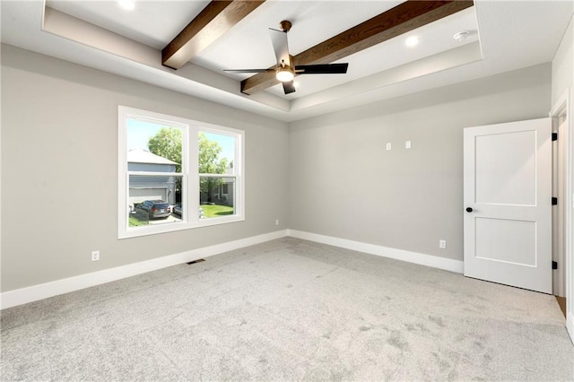 empty room featuring a raised ceiling, light carpet, ceiling fan, beamed ceiling, and baseboards