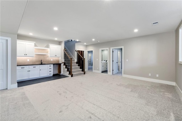 unfurnished living room with dark colored carpet, recessed lighting, visible vents, a sink, and stairs