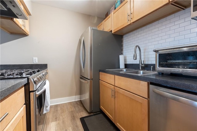 kitchen with appliances with stainless steel finishes, tasteful backsplash, wall chimney exhaust hood, sink, and light wood-type flooring