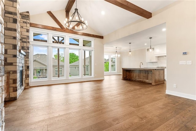 unfurnished living room featuring beamed ceiling, a fireplace, sink, hardwood / wood-style floors, and an inviting chandelier