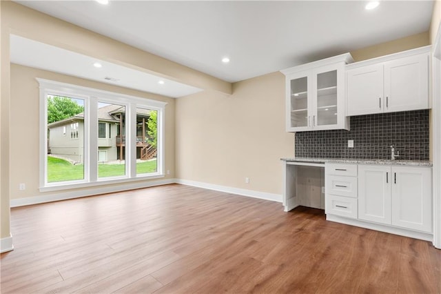 kitchen featuring backsplash, hardwood / wood-style flooring, light stone counters, white cabinets, and sink