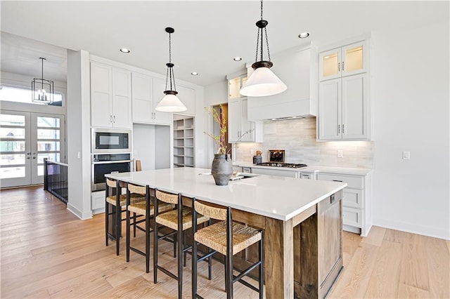 kitchen with decorative light fixtures, white cabinetry, a breakfast bar area, light hardwood / wood-style floors, and stainless steel appliances