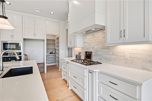 kitchen featuring hanging light fixtures, custom range hood, white cabinets, built in microwave, and stainless steel gas stovetop