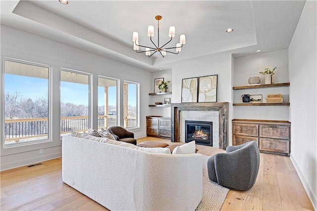 living room featuring a fireplace, light wood-type flooring, and a tray ceiling