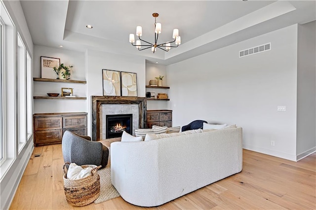 living room featuring a high end fireplace, a chandelier, light hardwood / wood-style floors, and a tray ceiling