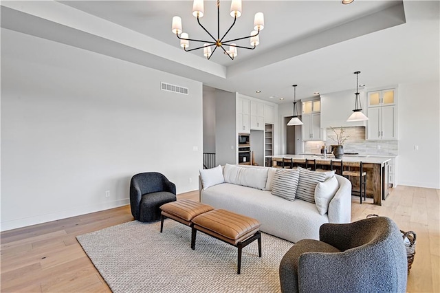 living room featuring a raised ceiling, an inviting chandelier, and light hardwood / wood-style floors