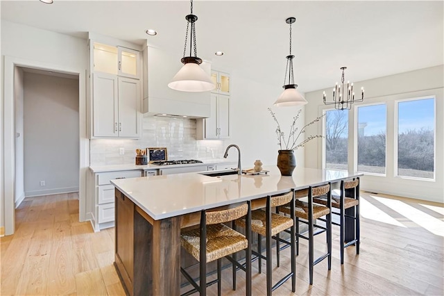 22051 W 100th Ter, Lenexa, KS 66220 - kitchen with an island with sink, backsplash, a sink, light wood-style floors, and light countertops