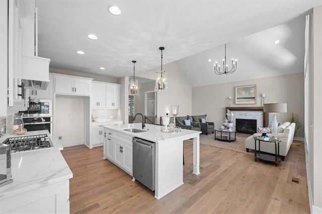 kitchen featuring pendant lighting, appliances with stainless steel finishes, a kitchen island with sink, light stone countertops, and white cabinets