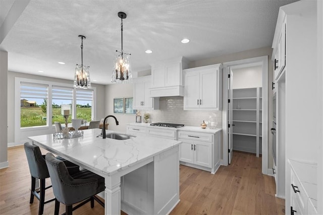 kitchen with white cabinetry, decorative light fixtures, a kitchen island with sink, and sink