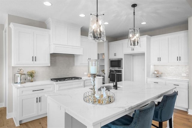 kitchen with stainless steel appliances, an island with sink, pendant lighting, and white cabinets