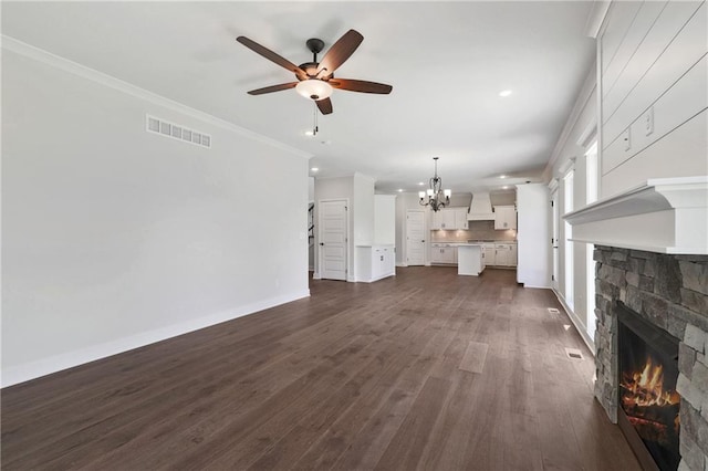 unfurnished living room featuring a fireplace, crown molding, ceiling fan with notable chandelier, and dark hardwood / wood-style flooring