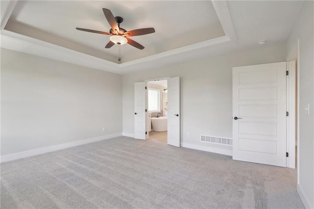 unfurnished bedroom with ceiling fan, carpet, a raised ceiling, and ensuite bathroom