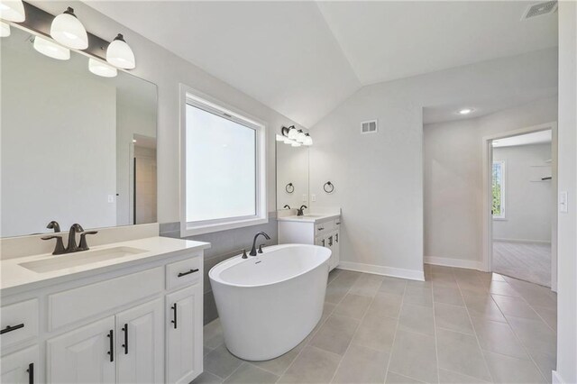 bathroom with a bath, vaulted ceiling, plenty of natural light, and dual bowl vanity