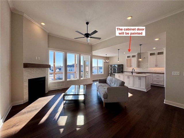 living room with sink, ceiling fan with notable chandelier, a high end fireplace, crown molding, and dark wood-type flooring