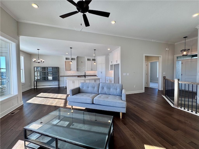 living room with ceiling fan with notable chandelier, dark wood-type flooring, and ornamental molding