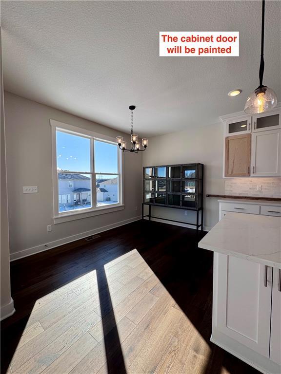 unfurnished dining area featuring a textured ceiling, a notable chandelier, and dark hardwood / wood-style floors