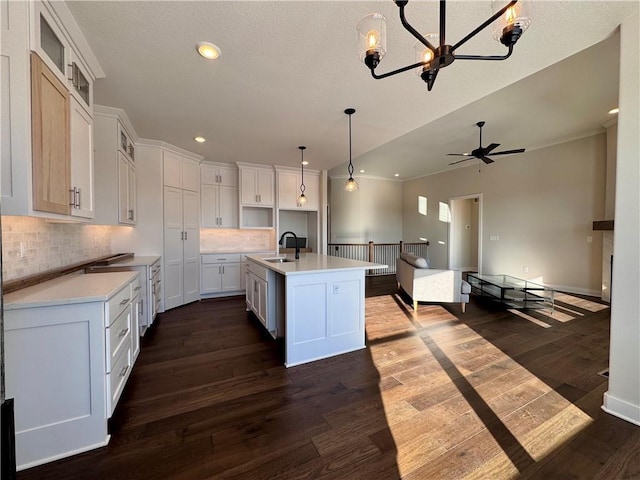 kitchen with sink, white cabinetry, decorative backsplash, a kitchen island with sink, and dark wood-type flooring