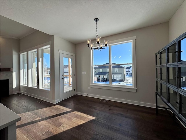 unfurnished dining area with dark wood-type flooring, a notable chandelier, a fireplace, and a healthy amount of sunlight