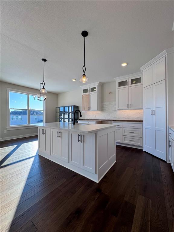 kitchen with a kitchen island with sink, dark wood-type flooring, decorative backsplash, white cabinetry, and decorative light fixtures