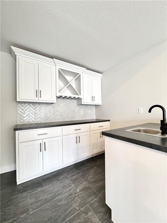 kitchen featuring a sink, dark countertops, a textured ceiling, and white cabinetry