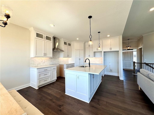 kitchen featuring dark wood finished floors, an island with sink, decorative backsplash, wall chimney exhaust hood, and a sink