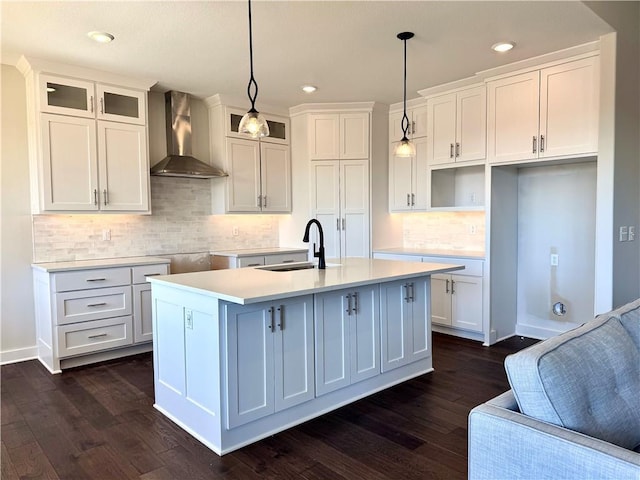 kitchen featuring a center island with sink, a sink, dark wood-style floors, white cabinetry, and wall chimney range hood