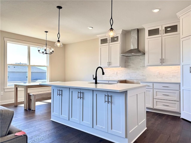 kitchen with tasteful backsplash, dark wood-type flooring, wall chimney range hood, pendant lighting, and a sink