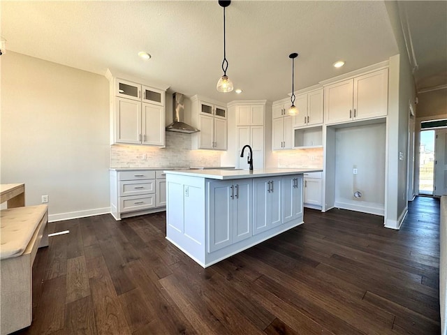 kitchen with a kitchen island with sink, tasteful backsplash, white cabinetry, wall chimney range hood, and dark wood-style flooring