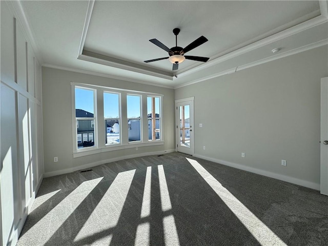 carpeted empty room featuring a tray ceiling, baseboards, a ceiling fan, and crown molding